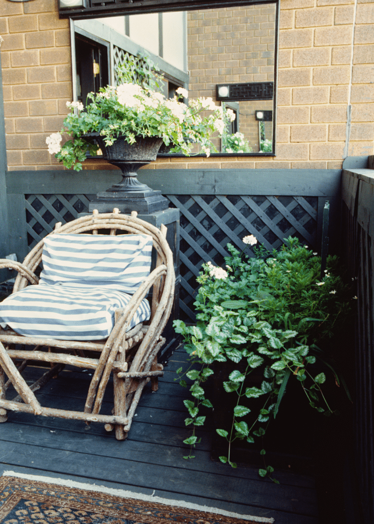 Small patio seating corner with a wooden chair, mirror, planters, and an outdoor rug.