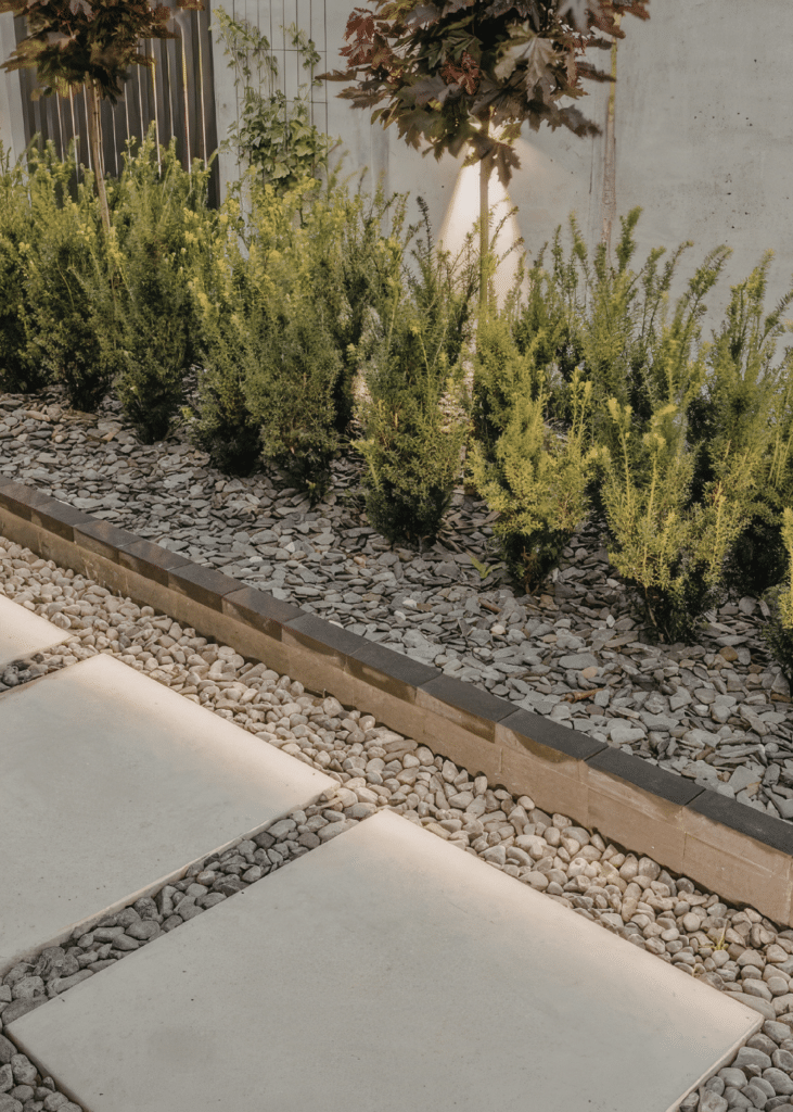 Narrow side yard with stone pavers set in gravel and a raised planting bed.