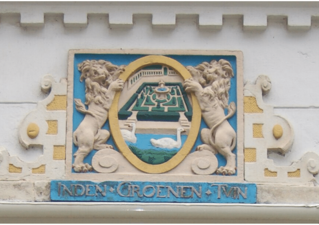 Decorative 17th‑century hofje entrance plaque showing two lions holding an oval frame with a formal garden scene and the inscription “Inden Groenen Tvin.”