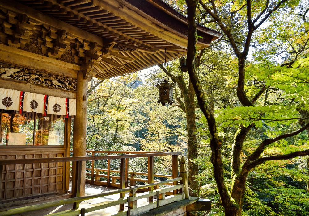 Horizontal photo of a rustic wooden Japanese house with a porch looking out over a lush, sylvan garden.